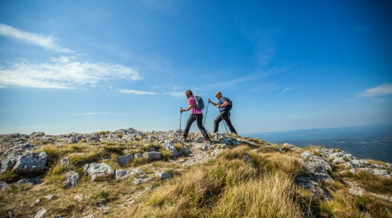 couple-hiking-nanos-plateau-slovenia-against-blue-sky